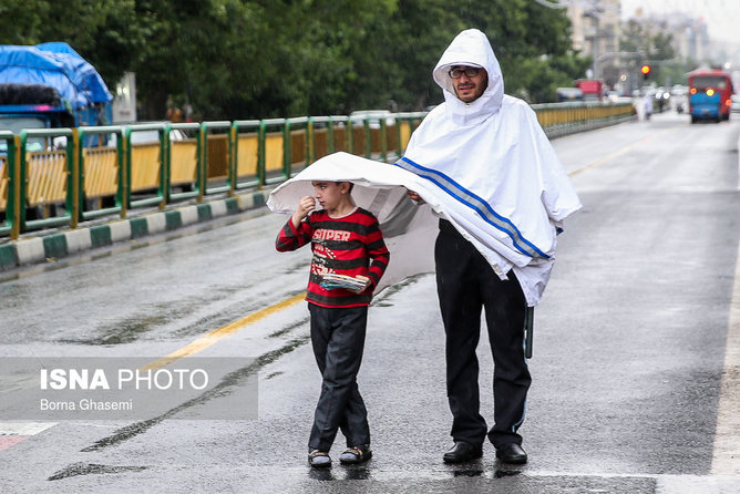 عکس منتخب سال -۲۲ اردیبهشت - در پی بارش باران بهاری در تهران یکی از پلیس های راهنمایی و رانندگی خیابان انقلاب تهران مانع خیس شدن کودک دستفروش می شود